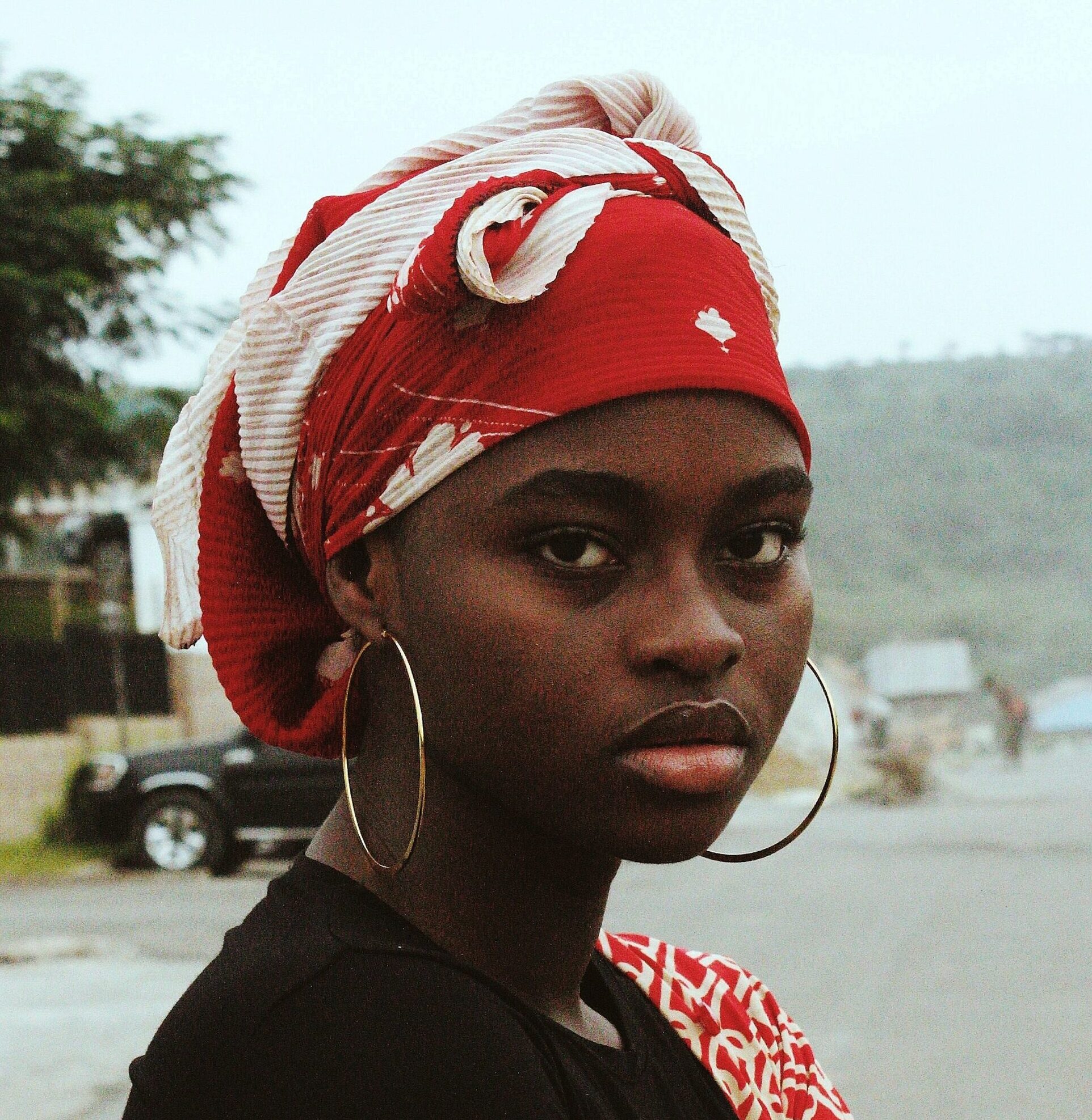 Stunning portrait of an African woman in Nigeria wearing a red headscarf and hoop earrings.
